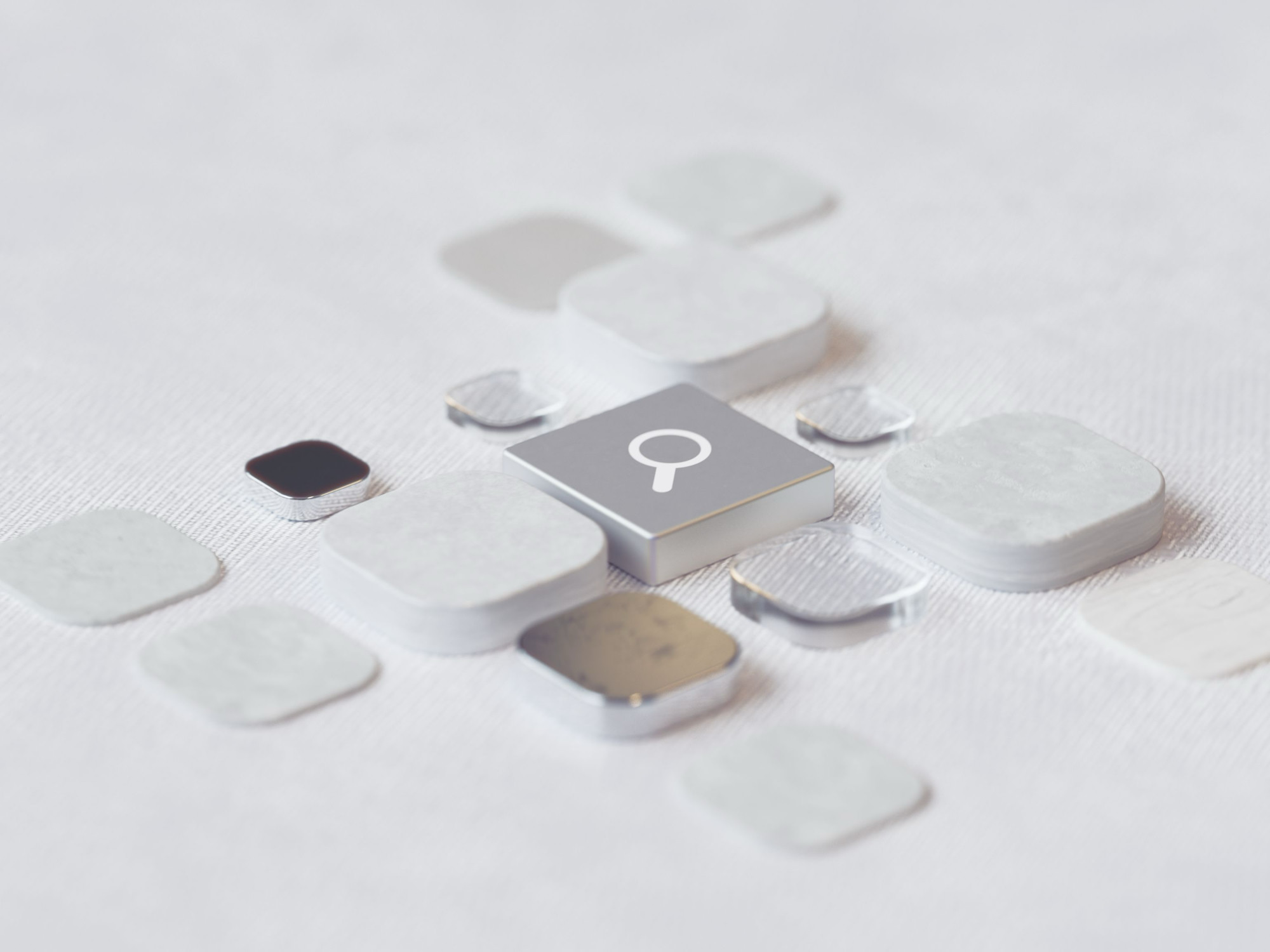 A metallic search-icon key at the center of a grid of blank white and silver app-style tiles on a textured surface