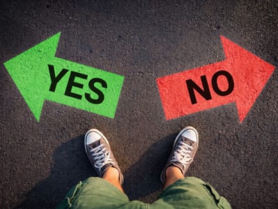 A person in green trousers stands on asphalt between a green arrow marked YES pointing left and a red arrow marked NO pointing right
